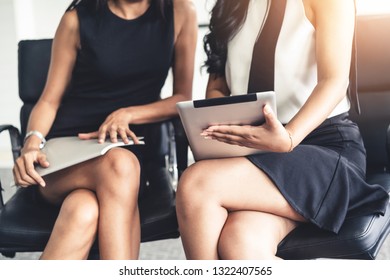 Two businesswomen discussing business while looking at financial data in their hands. They are sitting on the chairs in the office meeting room. - Shutterstock ID 1322407565