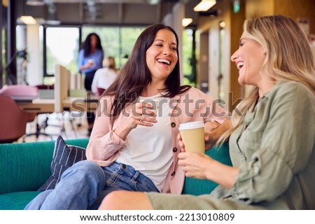 Two Businesswomen Having Informal Meeting In Breakout Seating Area Of Modern Office