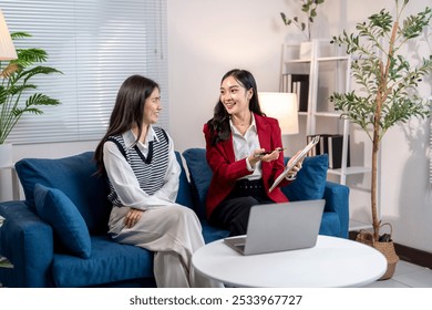 Two businesswomen are having a productive meeting in a modern office lounge, discussing using a laptop and taking notes on a clipboard - Powered by Shutterstock