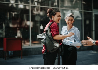 Two businesswomen laugh and engage in a joyful conversation outdoors during a work break, symbolizing camaraderie and teamwork. - Powered by Shutterstock