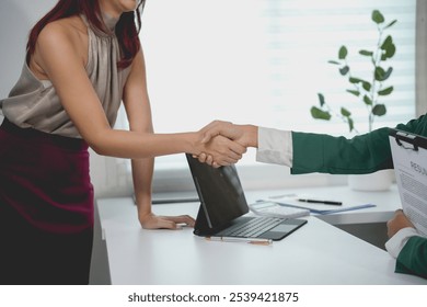 Two businesswomen in an office handshake, marking a successful job interview. Excitement fills the air as they begin a promising partnership. Confidence and professionalism shine in their attire - Powered by Shutterstock