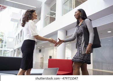 Two Businesswomen Shaking Hands In Lobby Of Modern Office