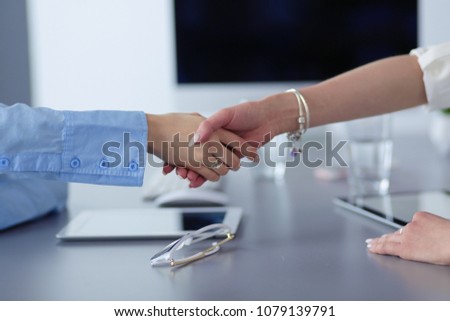 Two businesswomen sitting at a desk shaking hands