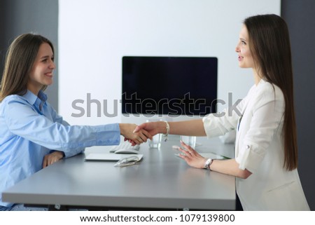 Two businesswomen sitting at a desk shaking hands