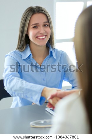 Two businesswomen sitting at a desk shaking hands