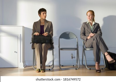 Two businesswomen sitting in office reception area side by side and waiting patiently. - Powered by Shutterstock