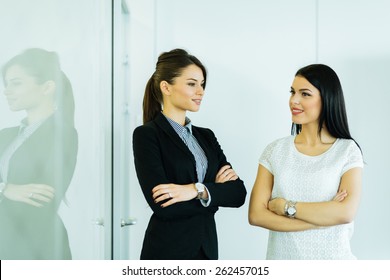 Two Businesswomen Talking In An Office With Reflection Showing On The Glass Wall Next To Them