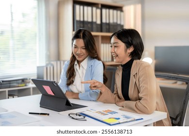 Two businesswomen are working together in the office, analyzing financial charts on a digital tablet - Powered by Shutterstock