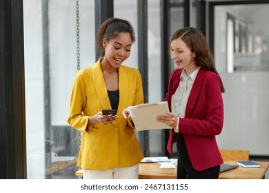 Two businesswomen working together using documents Work files talk about business projects. Creative team of African American female executives stand meeting in modern office. - Powered by Shutterstock