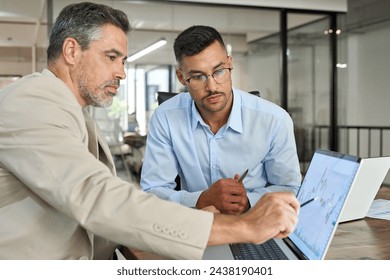Two busy business men investors doing financial trading market data analysis. Male advisor and analyst consulting about stock exchange investing pointing at chart on laptop computer working in office.