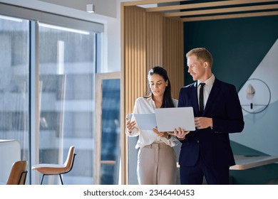 Two busy diverse coworkers discussing project walking in office with laptop and documents. International business team people colleagues standing having teamwork conversation. Authentic shot - Powered by Shutterstock