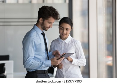 Two Busy Diverse Young Business Coworkers In Formalwear Using Tablet Computer, Watching Online Presentation. Employees Discussing Startup Project. Indian Professional Consulting Colleague Expert