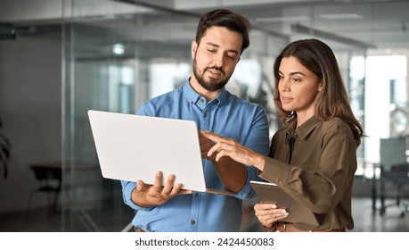 Two busy professional business people working in office with computer. Middle aged female executive manager talking to male colleague having conversation showing software online solution on laptop.
