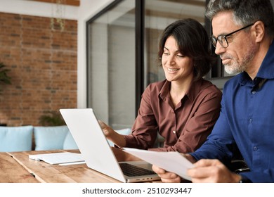 Two busy professionals man and woman business executives checking document working together on laptop in office. Financial advisor manager lawyer and investor discussing corporate project at meeting.