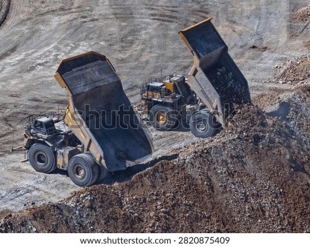 Two CAEX haul trucks simultaneously dumping material from an open-pit mine, aerial view