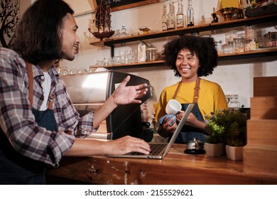 Two cafe business startup partners and friends, African American female, and Thai male baristas talk and cheerful smile together at counter bar of coffee shop, happy service job, and SME entrepreneur. - Powered by Shutterstock