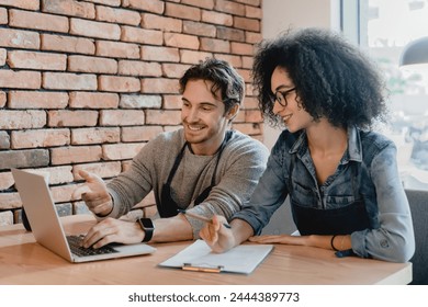 Two cafeteria staff working on laptop and writing down together in loft cafeteria. Educational promotional training for staff, e-learning for shop assistants in restaurant. New trainees - Powered by Shutterstock