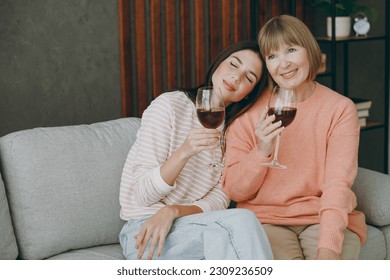 Two calm adult women mature mom young kid wear casual clothes drink wine put head on shoulder sit on gray sofa couch stay at home flat rest relax spend free spare time in living room. Family concept - Powered by Shutterstock