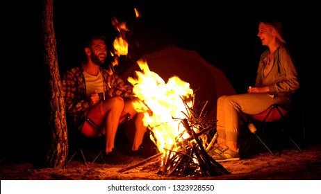 Two campers warming up near campfire, telling funny stories, wild fire risk