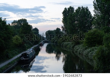 Two canal boats on river at dusk surrounded by trees beautiful sunset reflected in still fresh water in summer