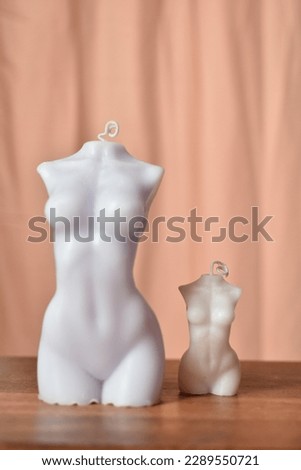 two candles, small and large in the form of a naked female body,
    on a wooden table