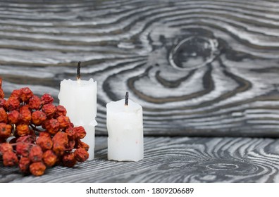 Two candlesticks on brushed pine boards. Nearby is a dried rowan bunch.