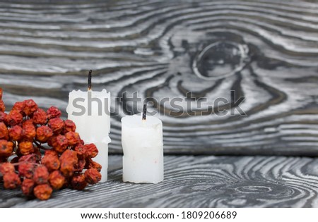 Two candlesticks on brushed pine boards. Nearby is a dried rowan bunch.