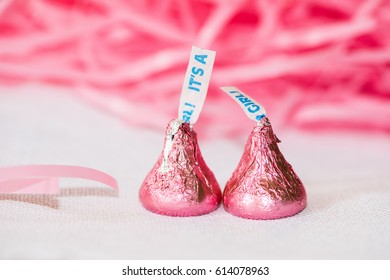 Two Candy Kisses wrapped in pink foil with a tag at the top to announce that "Its a girl" as a baby announcement. Background is pink confetti.horizontal.