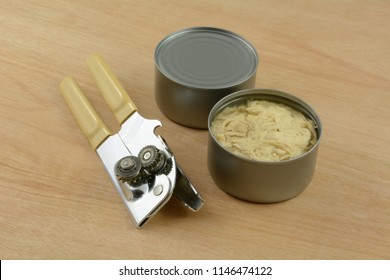 Two Cans Of Albacore Tuna Fish With Manual Can Opener On Wooden Table