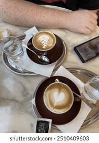Two Cappucino Cups On Trays On Marble Table