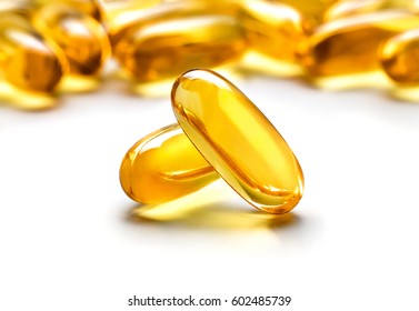 Two capsules Omega 3 isolated on white background and many other of capsules on blurred background. Close up, high resolution product. Health care concept