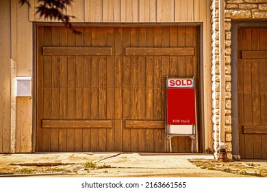 Two Car Garage With Rustic Wooden Doors With For Sale Sign Saying Sold Propped Up Against It - Copy Space