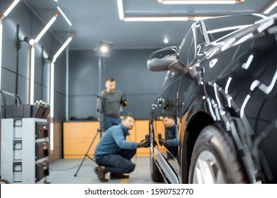 Two Car Service Workers Examining Vehicle Body For Scratches And Damages While Taking A Car For Professional Automotive Detailing