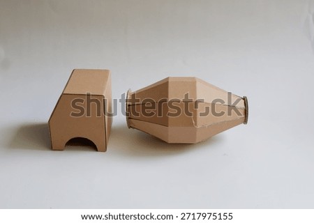 Two cardboard structures, one rectangular and one conical, against a plain white background. Edges and creases highlight their material, under neutral lighting.