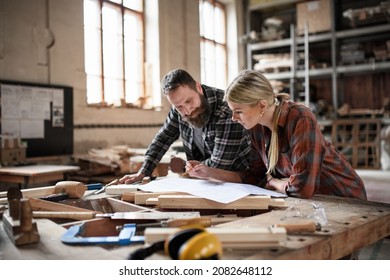 Two carpenters man and woman looking at blueprints indoors in carpentery workshop. - Powered by Shutterstock