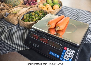 Two carrots are weighed on a digital scale. Equipment of a small outdoor stall at a public market. - Powered by Shutterstock