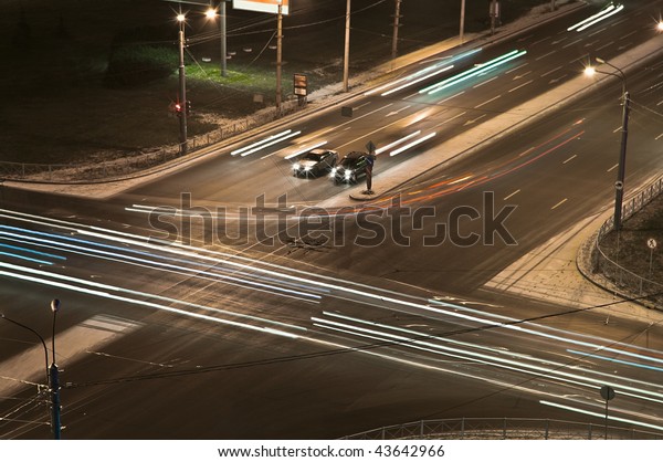 Two cars at a crossroads wait at night a green\
signal of a traffic light. Night shooting. Bright traces of\
headlights of cars