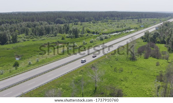 two cars drive each other along the\
road that is surrounded by forests, lakes, fields and meadows.\
retro cars and modern minivans travel in summer. aerial view\
