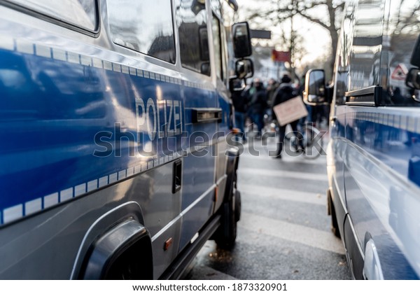 Two cars of german police besides a\
demonstration in Bremen against the corona-laws. In the blurry\
background is a protester on a bike with an protest\
sign.