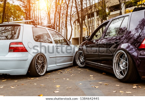 Two cars\
white blue and purple want to take one parking space. Parking\
problems in the city. Parked tightly to each other. Snuggled\
bumper. Low tuned cars with forged custom\
wheels