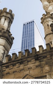 Two castle like structures frame a view of a modern high rise building. The scene shows a mix of old and new architecture under a clear sky during daytime.