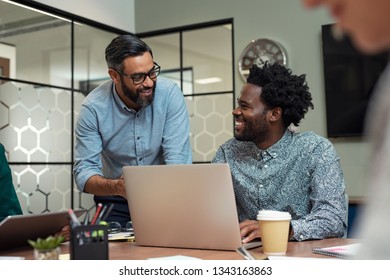 Two casual business partners sitting at table together and working. Group of smiling creative businesspeople working together. Mature businessman discussing affairs with african man in a meeting room.