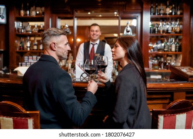 Two casual business people in a hotel bar in the evening talking while having two glasses of red wine after check-in. Horizontal shot. Selective focus