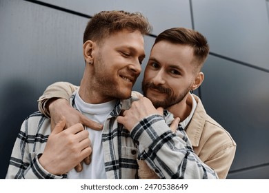 Two casually dressed men stand next to each other near a building, enjoying each others company.
