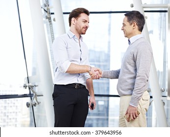 Two Caucasian Business Executives In Casual Wear Shaking Hands In Office.