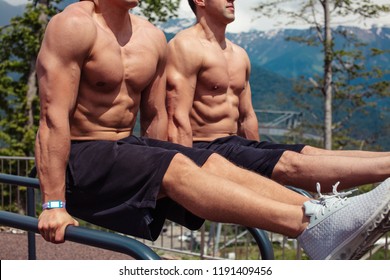 Two caucasian fit man workout out arms on dips horizontal bars training triceps and biceps doing push ups outdoors.