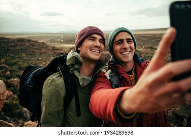 Two caucasian male friends taking selfie with cellular device standing on top of mountain enjoying the view
