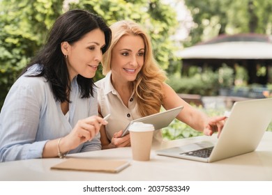 Two Caucasian Middle-aged Businesswomen Best Friends Colleagues Working Together On Laptop, E-learning, Remote Job, Business Partners Dealing In City Cafe. New Startup, Business Project Concept.