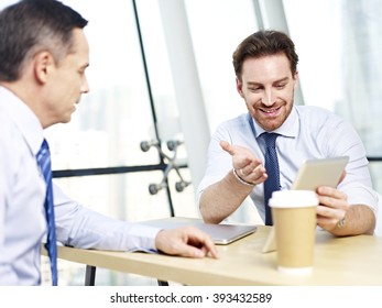 Two Caucasian Office People Discussing Business Using Tablet Computer In Office.