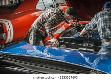 Two Caucasian Professional Classic Cars Mechanics Looking Under Muscle Car Hood